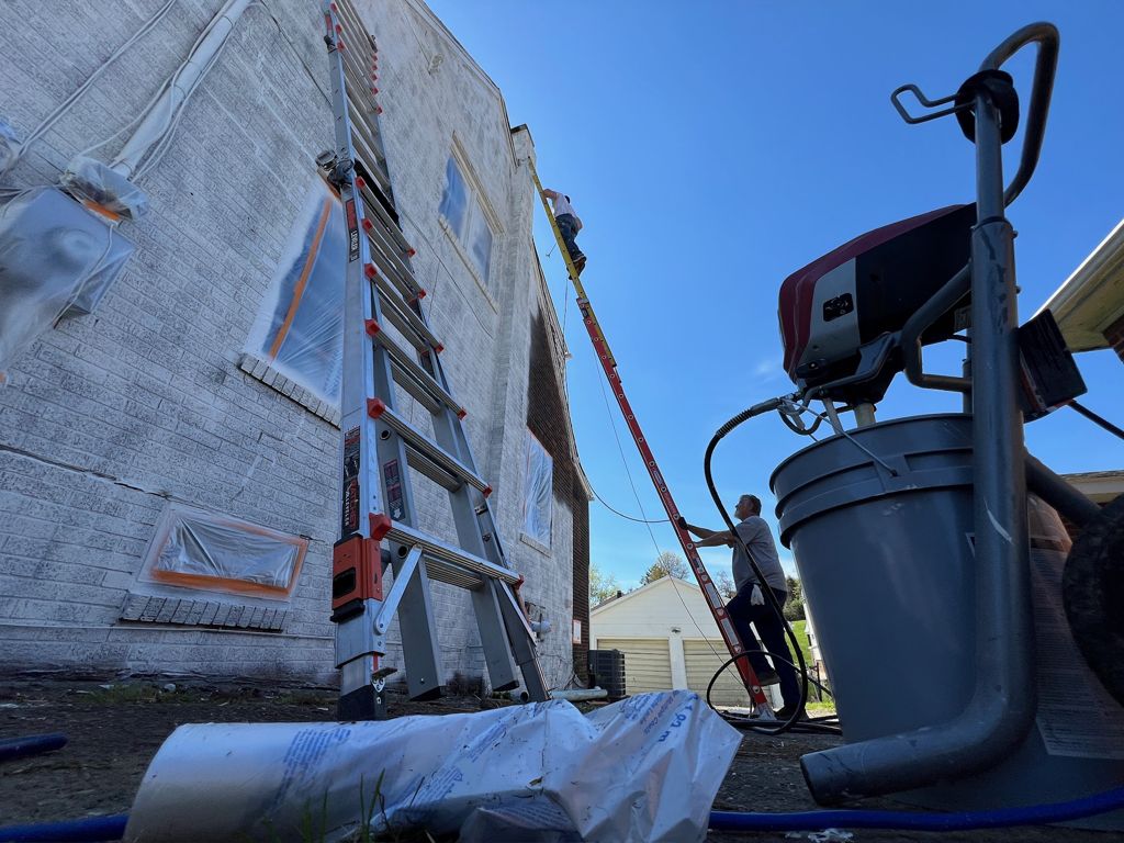 Painter spraying a building exterior from a ladder